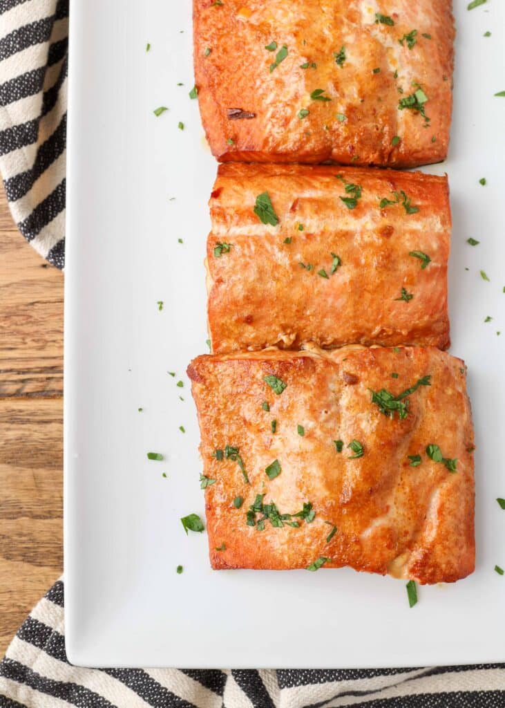 caramelized cooked salmon filets on a white plate with chopped parsley garnish