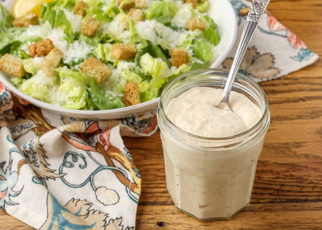 jar of salad dressing with spoon next to salad on table