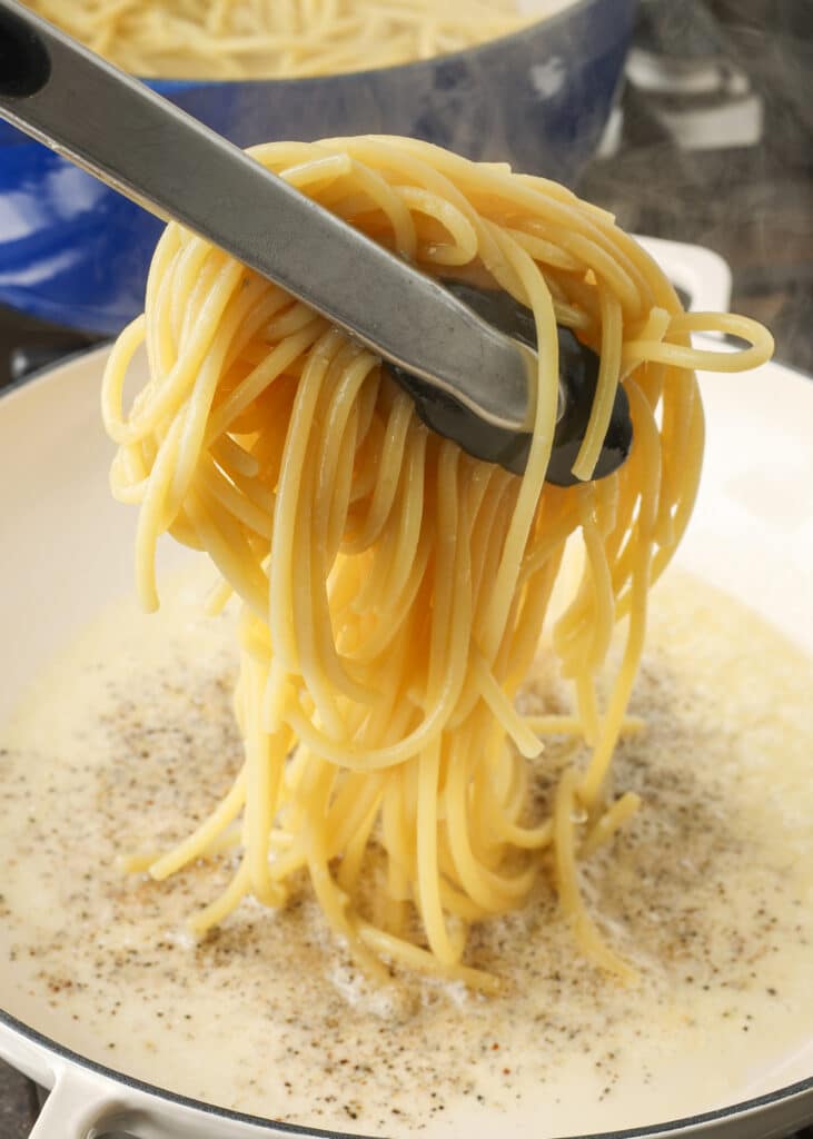 transferring cooked spaghetti to pepper and butter sauce