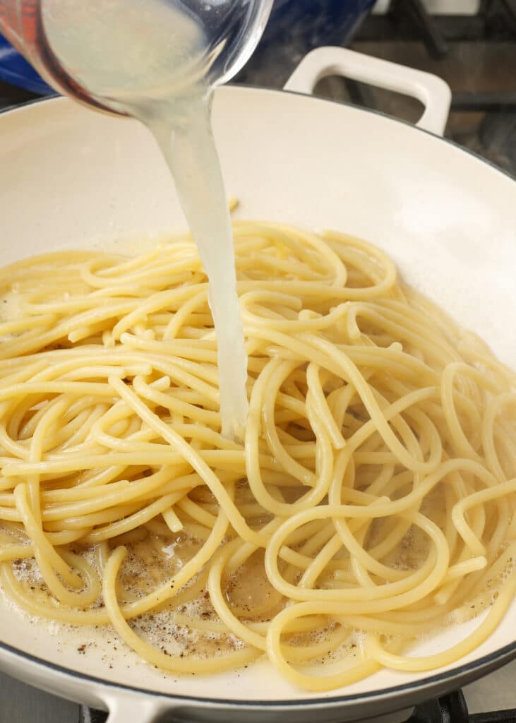 adding pasta water to cooked spaghetti in parmesan pepper pasta