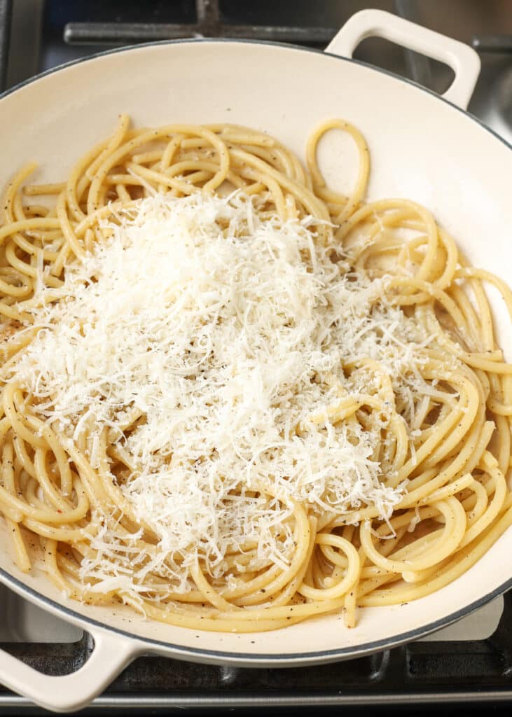 spaghetti being tossed with parmesan cheese in a bowl