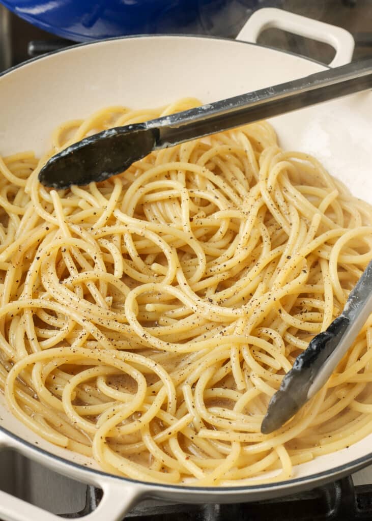 spaghetti being tossed with pepper in a pan