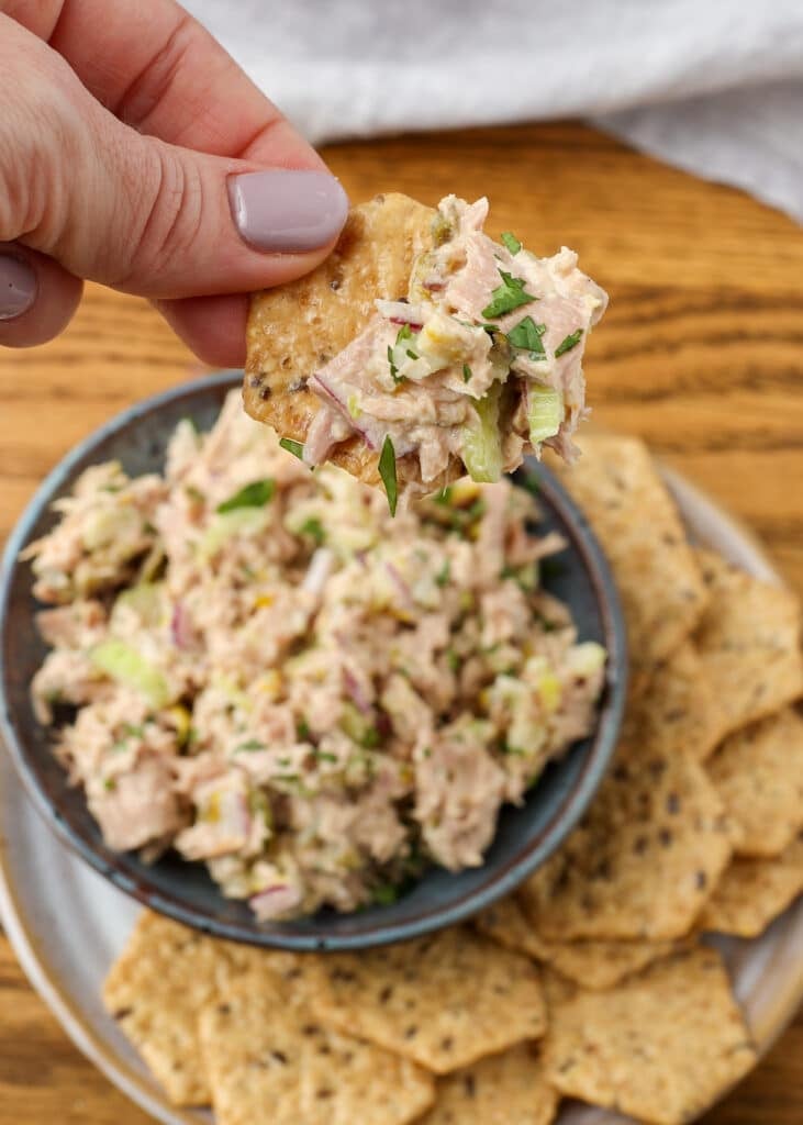 a hand holding spicy tuna salad on a cracker