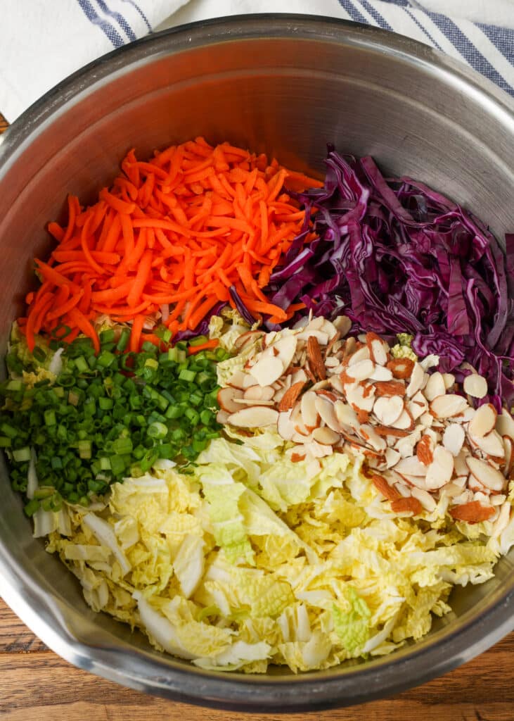 multi color Asian cabbage salad in a mixing bowl on a wooden surface with a blue and white linen