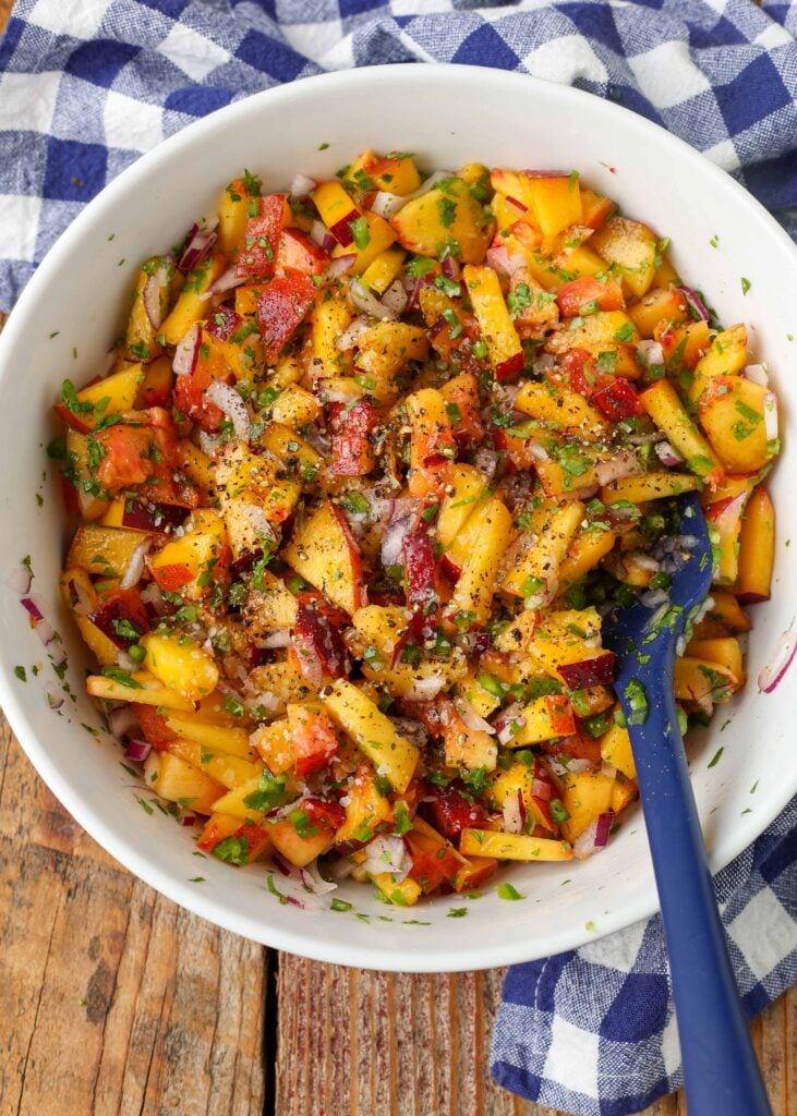 white mixing bowl holding peaches, jalapenos, cilantro, and onions