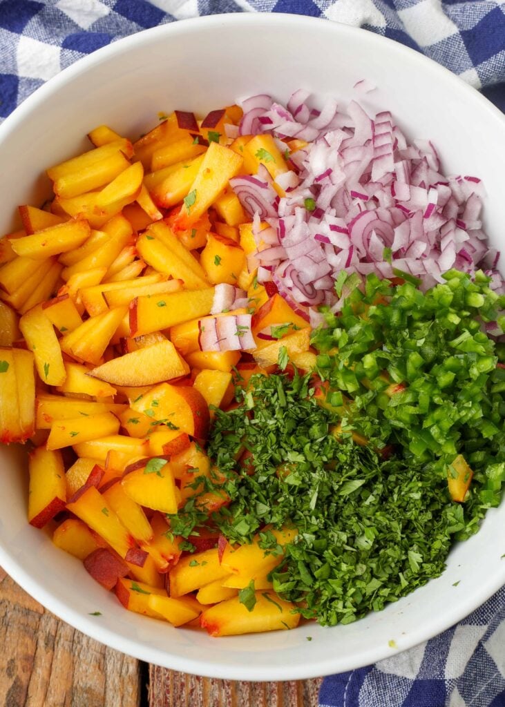 mixing bowl holding peaches, jalapenos, cilantro, and onions next to blue and white napkin