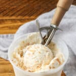container of ice cream on wooden table with scoop