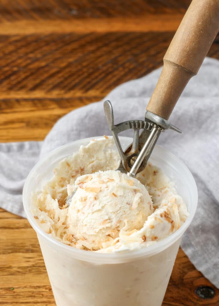 container of ice cream on wooden table with scoop 
