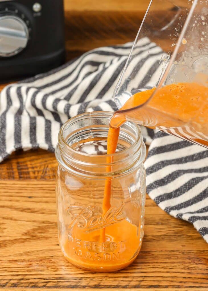 pouring asian salad dressing in a mason jar with a striped linen