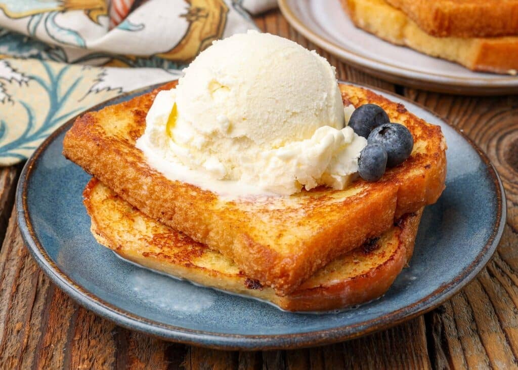 horizontal shot of french toast stacked on plate topped with scoop of ice cream