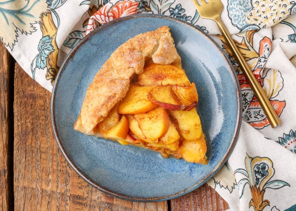 rustic style galette filled with peaches on blue plate with gold fork