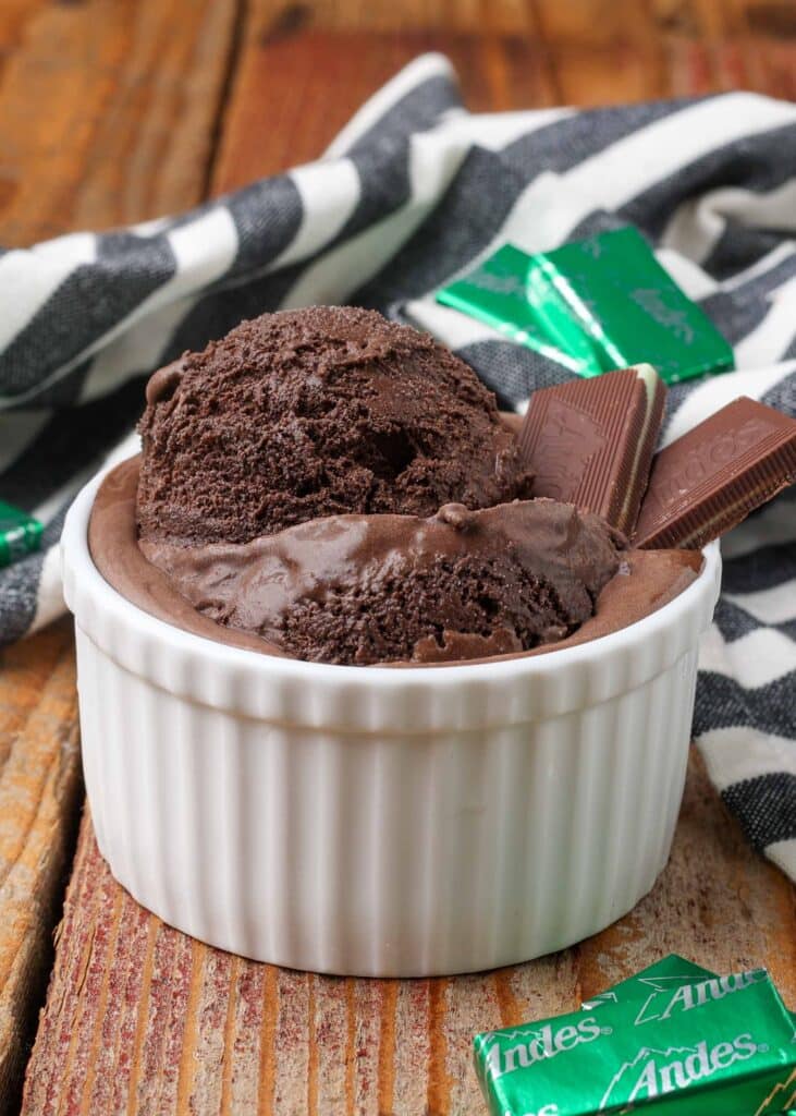 white dish holding large scoop of Andes mint ice cream with mints on table next to bowl