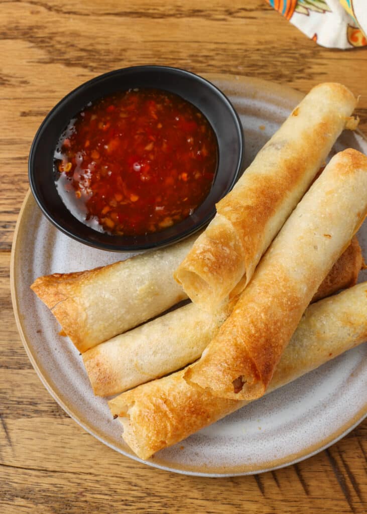 lumpia rolls on white plate with bowl of dipping sauce