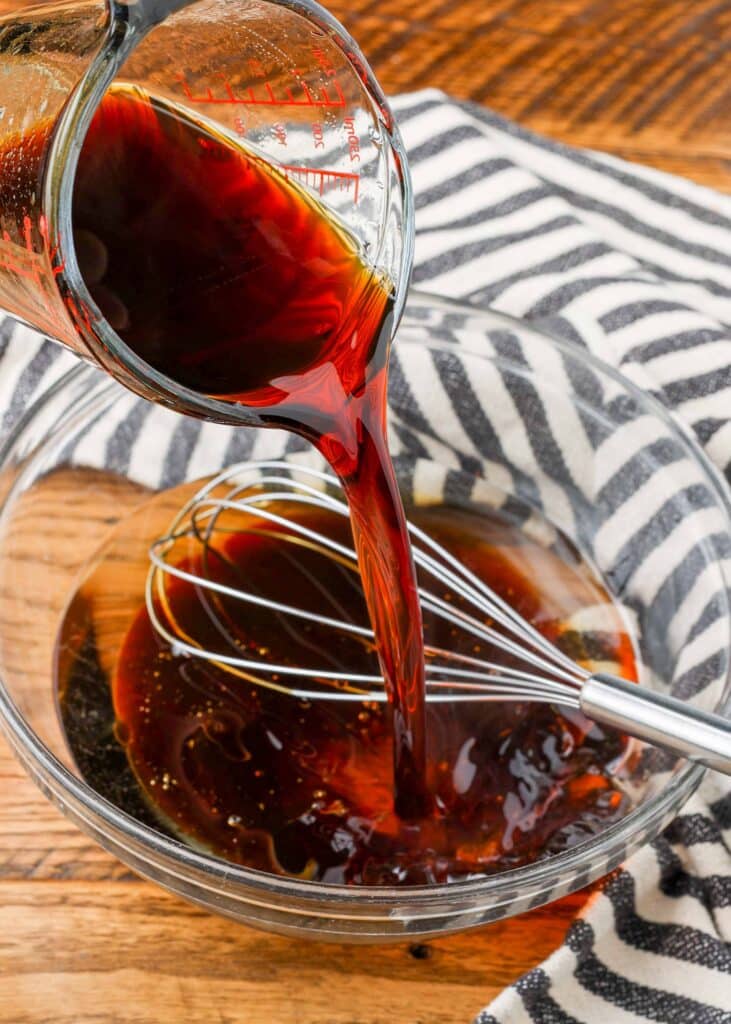 pouring tamari into a bowl with a whisk to make dressing