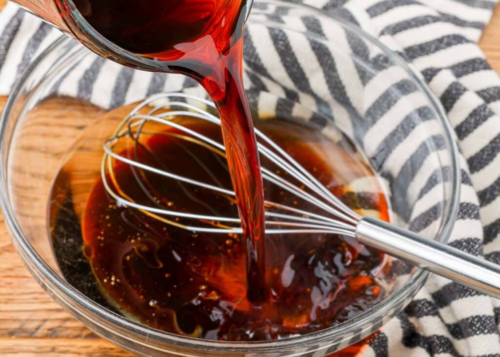 pouring tamari into a bowl with a whisk to make dressing