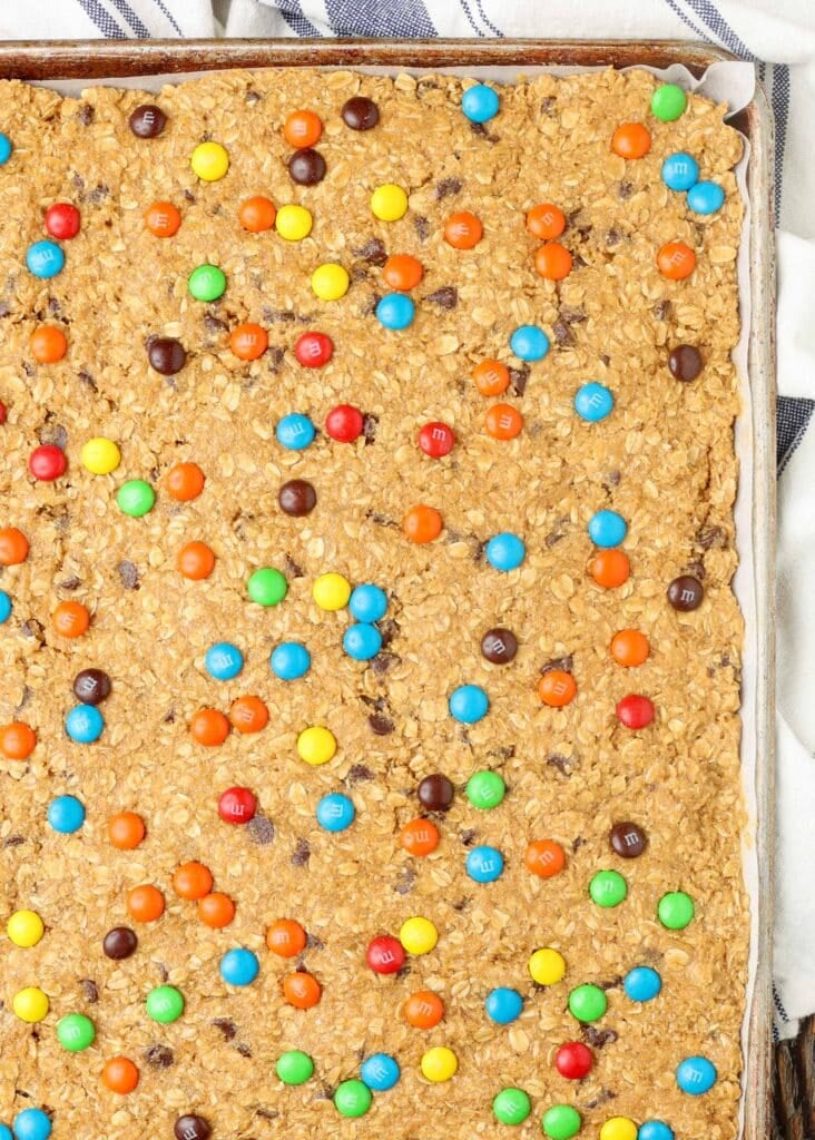 unbaked cookie bar batter pressed into sheet pan and topped with m&ms