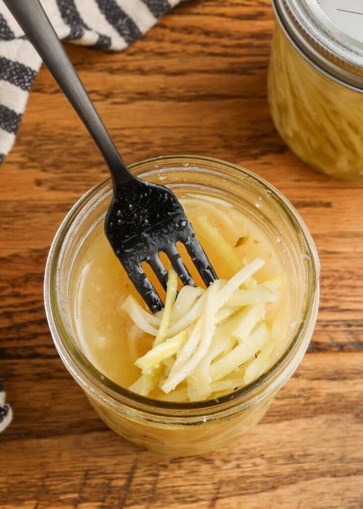 pickled broccoli stems in a jar of brine with a fork