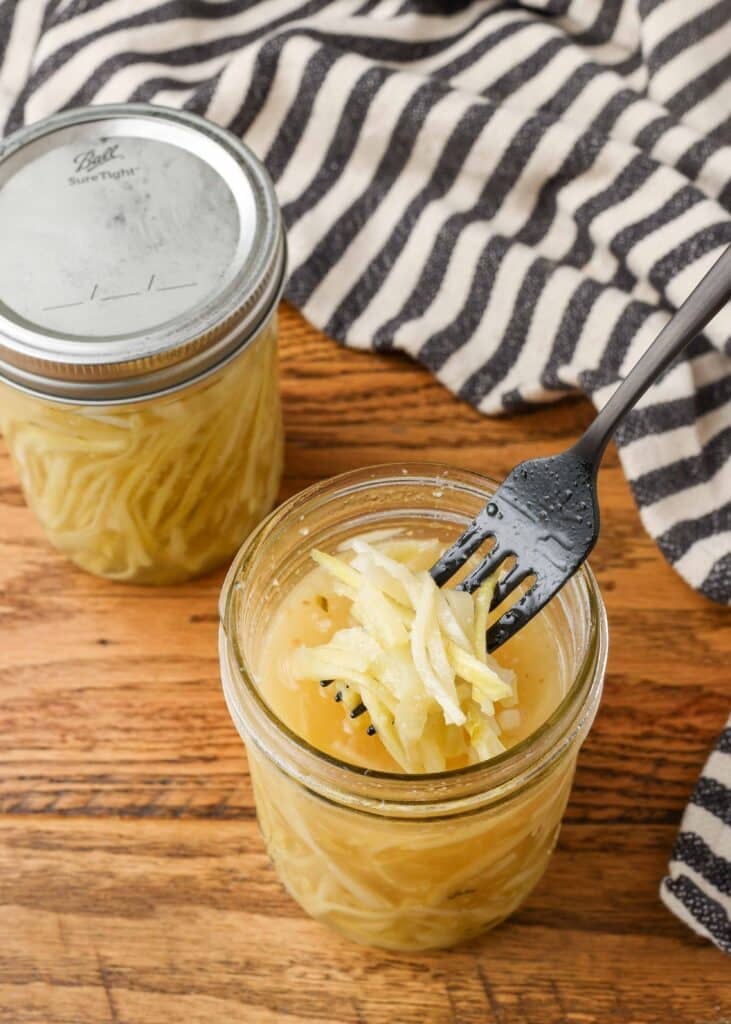pickled broccoli stems in a jar of brine with a fork