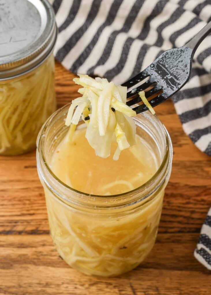 pickled broccoli stems in a jar of brine with a fork