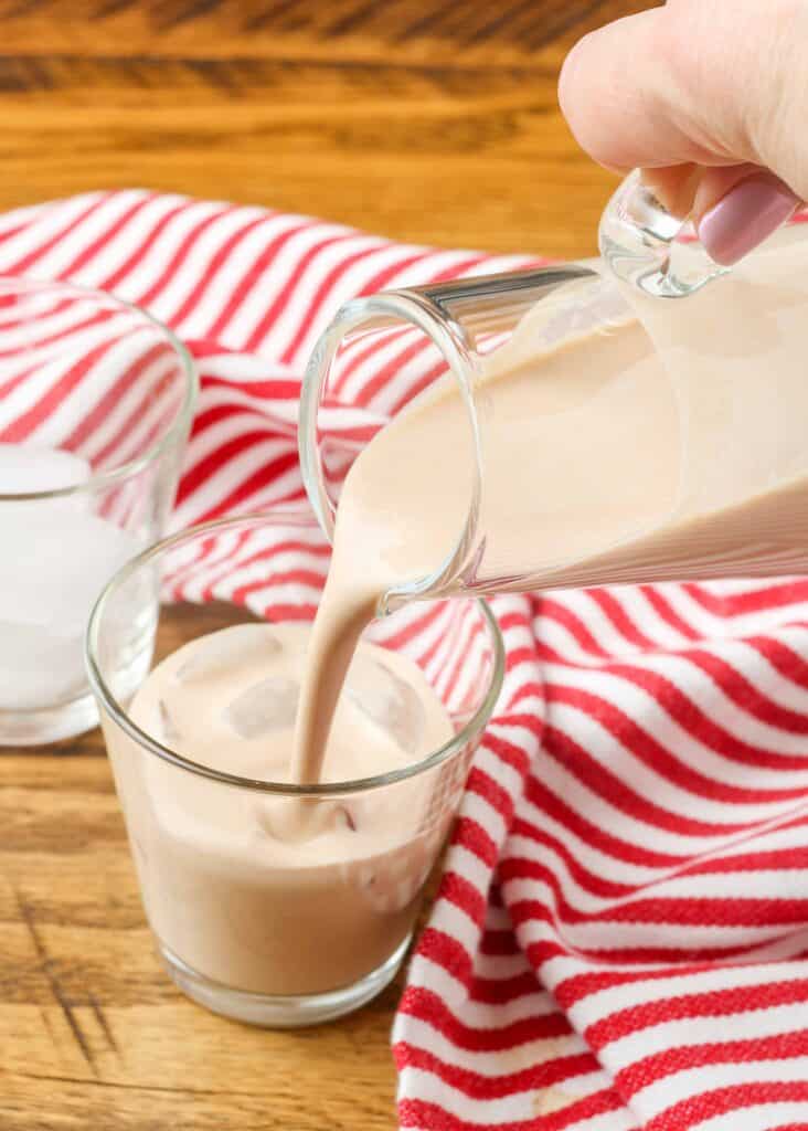 pouring homemade irish cream into a shot glass by a red and white striped linen