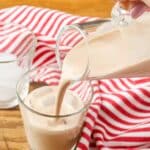 pouring homemade irish cream into a shot glass by a red and white striped linen