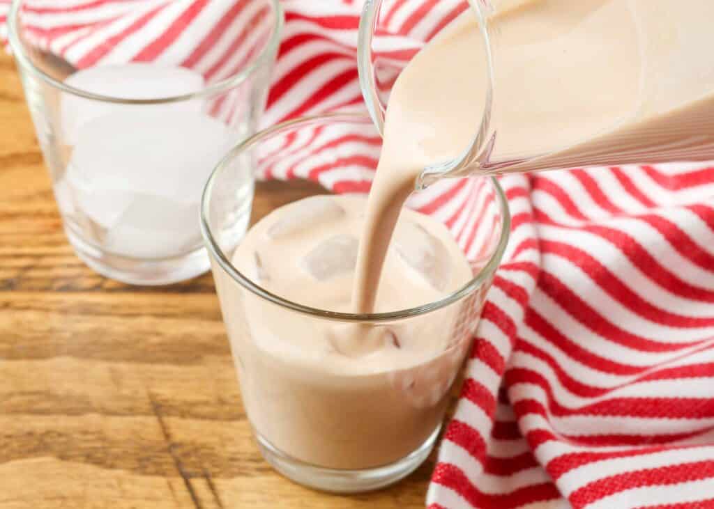 pouring homemade irish cream into a shot glass by a red and white striped linen