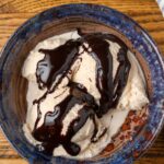 Homemade Bailey's ice cream with chocolate sauce in a blue pottery bowl with a blue and white striped linen