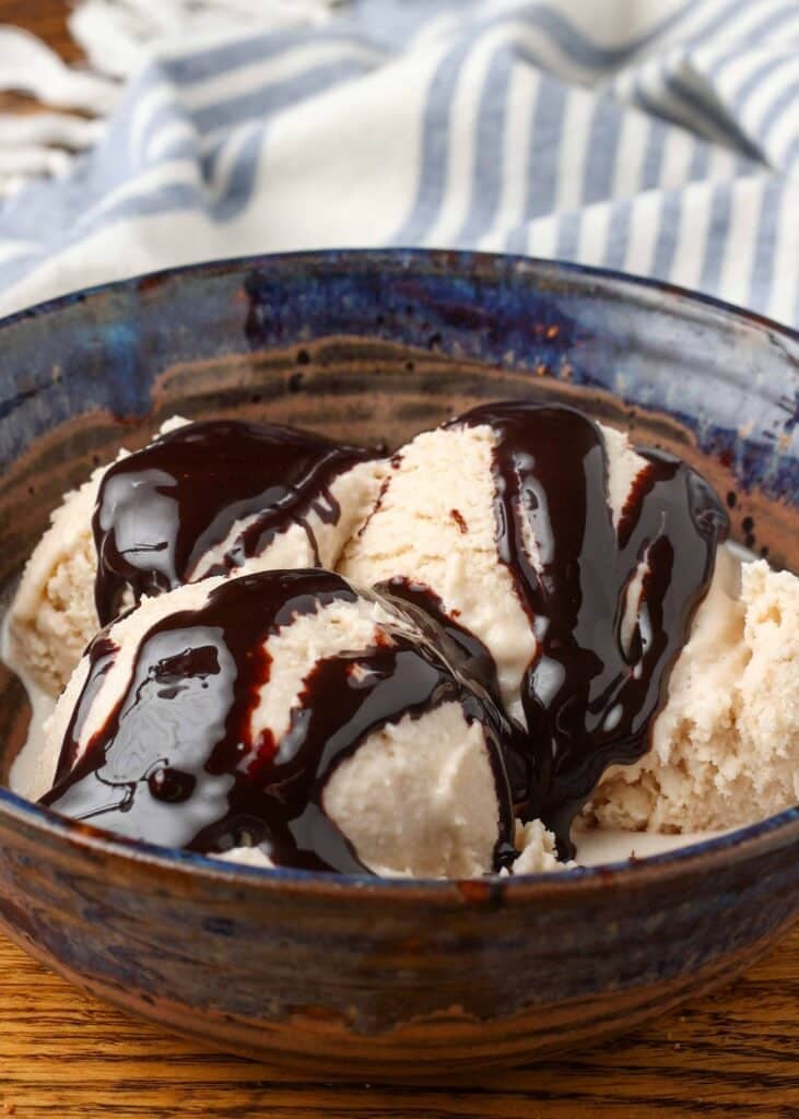 Homemade Bailey's ice cream with chocolate sauce in a blue pottery bowl with a blue and white striped linen