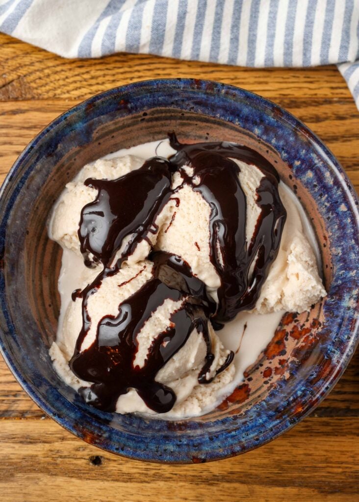 Homemade Bailey's ice cream with chocolate sauce in a blue pottery bowl with a blue and white striped linen