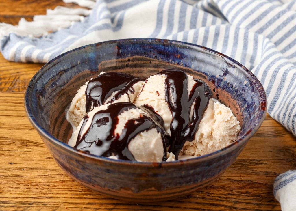 Homemade Bailey's ice cream with chocolate sauce in a blue pottery bowl with a blue and white striped linen