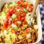 frito pie casserole topped with lettuce, tomatoes, and cilantro in a baking dish