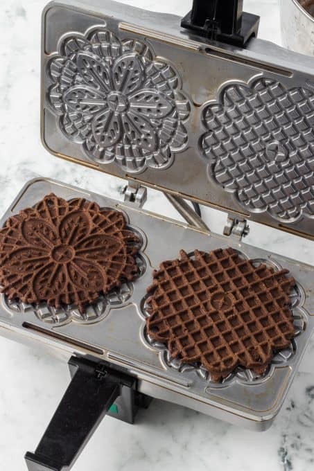 A pizzelle maker with chocolate cookies.
