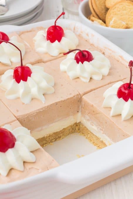 Looking into a pan with a slice taken out of Root Beer Dream Bars with whipped cream and cherries on top.