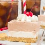 A layered dessert with whipped cream, a long stem cherry, and red and white drinking straw on top.