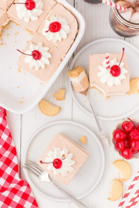 Looking down at a light brown gelatin dessert topped with whipped cream and long stem cherries.