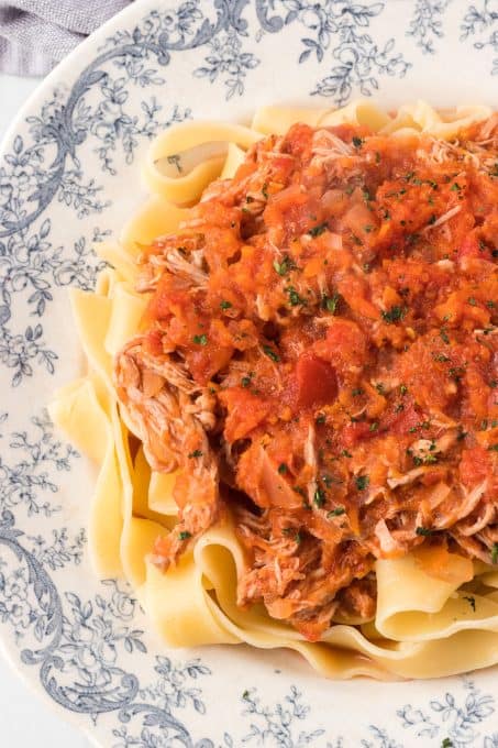 A plate of tomato sauce with shredded meat over long, thin noodles.