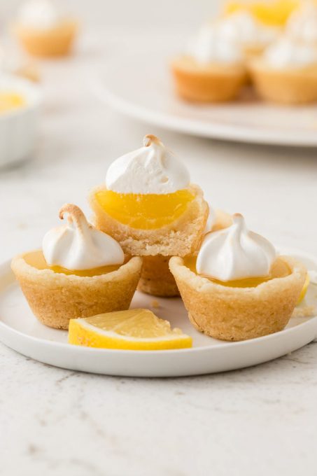 Cookie cups with meringue topping on a plate with a slice of lemon.