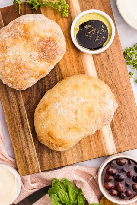 Two loaves of bread on a cutting board with a bowl of olive oil dipping sauce.