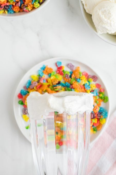 Decorating the rim of a milkshake glass with colorful rice cereal.