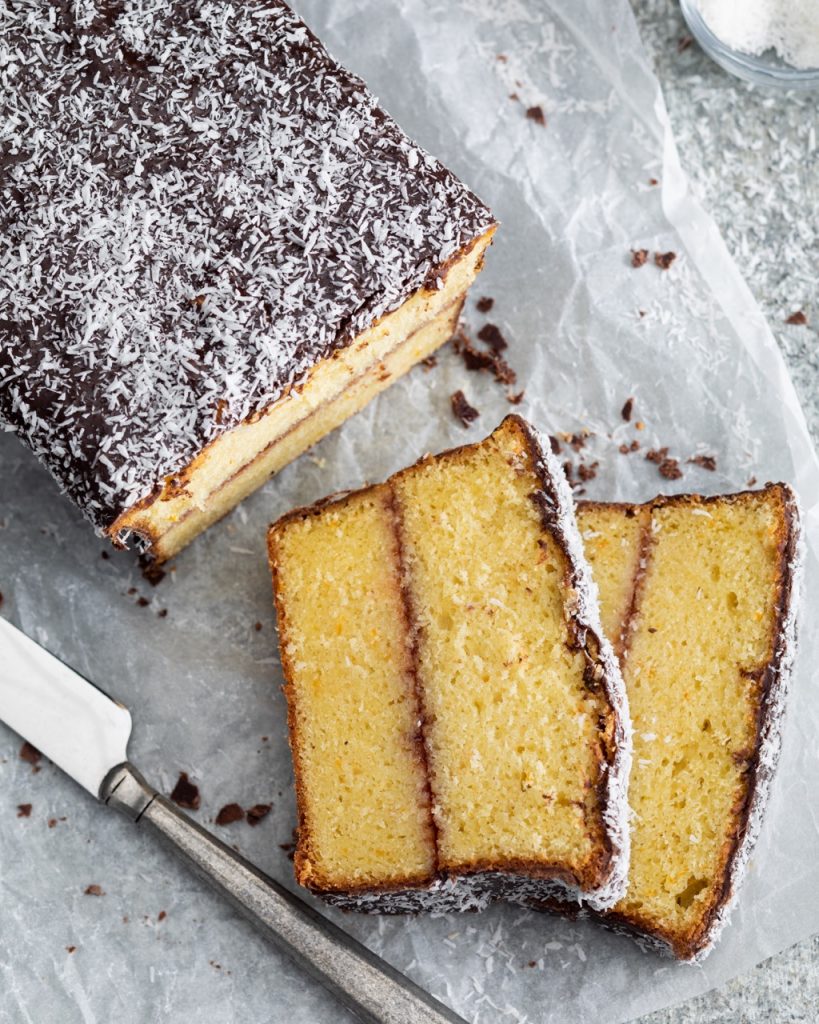 Orange-Plum Lamington Loaf Cake sliced on parchment