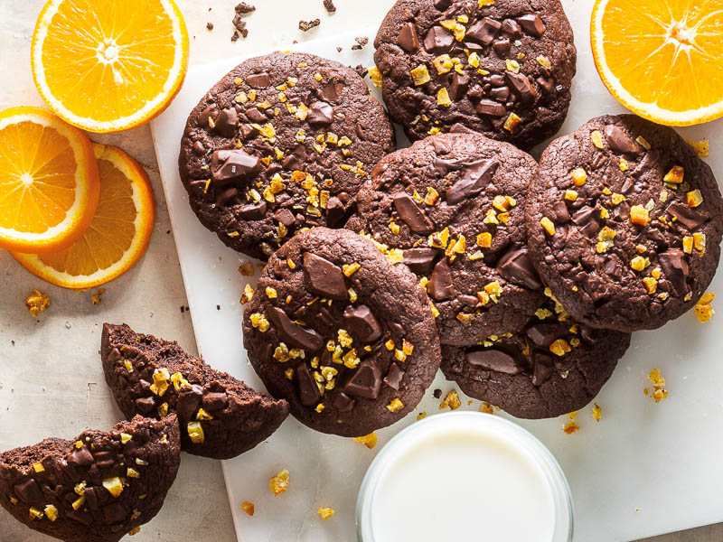 Orange-Chocolate Brownie Cookies stacked on white marble overhead with orange slices