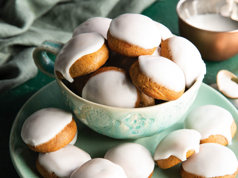 Pfeffernusse on green surface piled into a bowl and scattered on a plate.