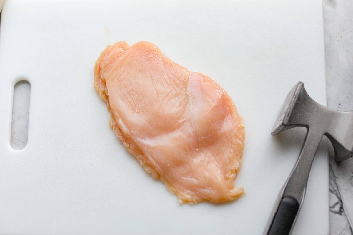 Pounded chicken breast on a cutting board next to a meat mallet 