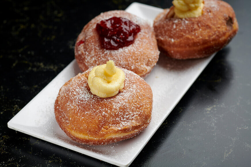 Three Italian bomboloni with cream and marmalade on a white plate.