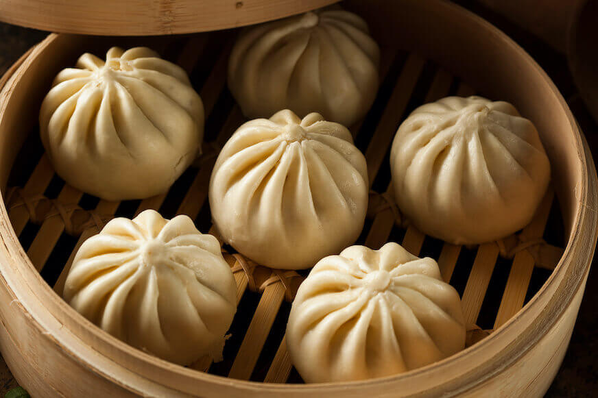 Six steamed barbeque pork bao sit in a bamboo basket