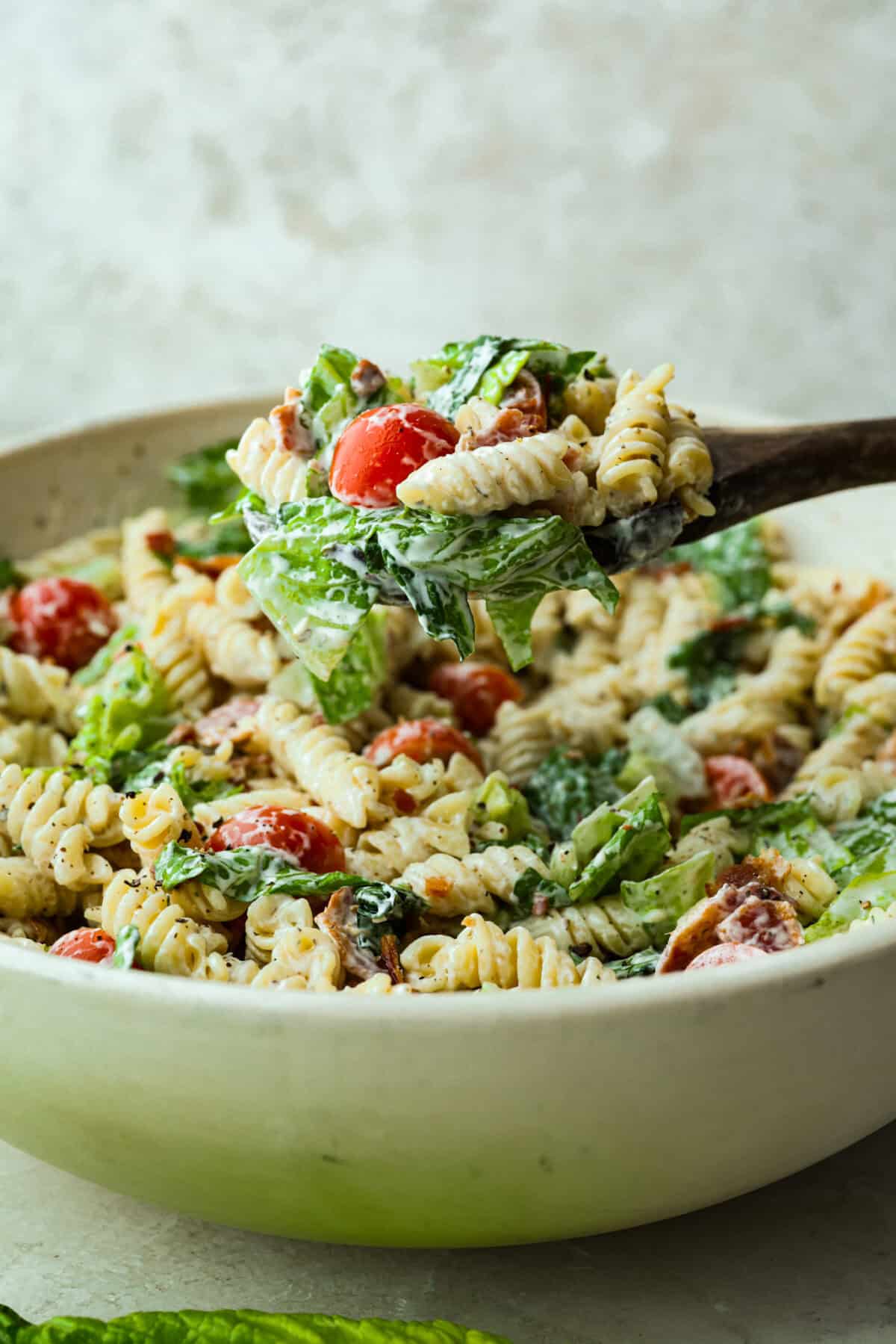 Someone lifting a scoop of BLT pasta salad out of the large pasta bowl. 