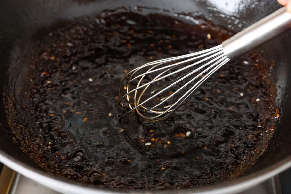 An shot of boiling sauce and oil and garlic in a skillet with someone whisking it. 