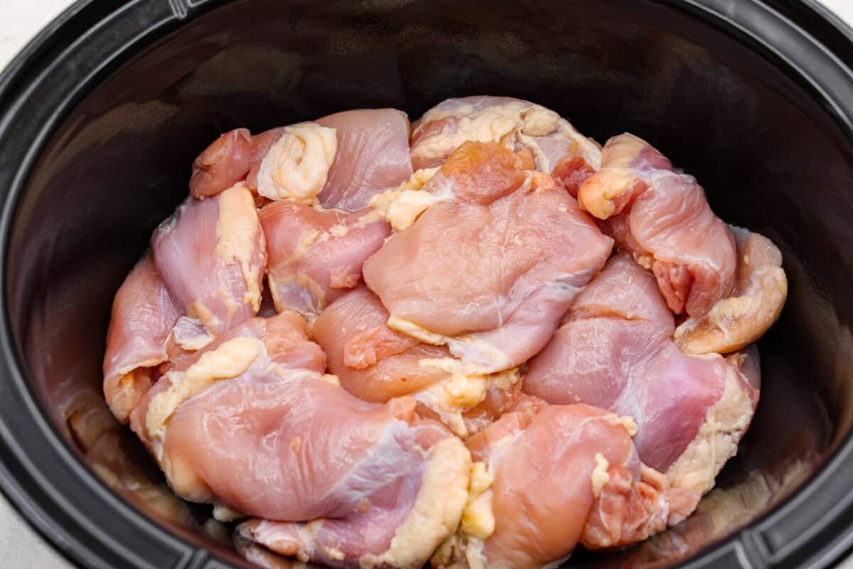 Chicken thighs added to the bottom of the slow cooker.