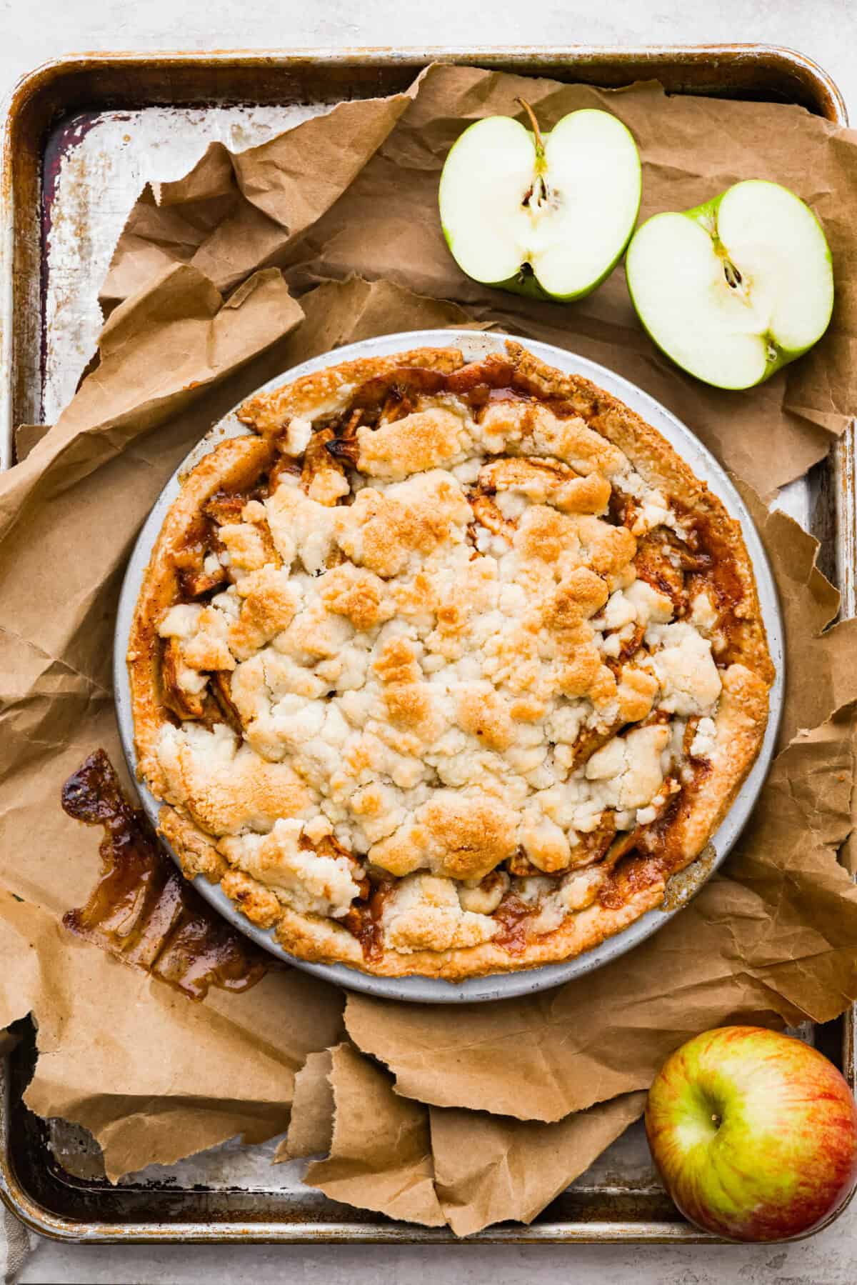 Overhead shot of baked brown bag apple pie on a cookie sheet with a green apple cut in half.