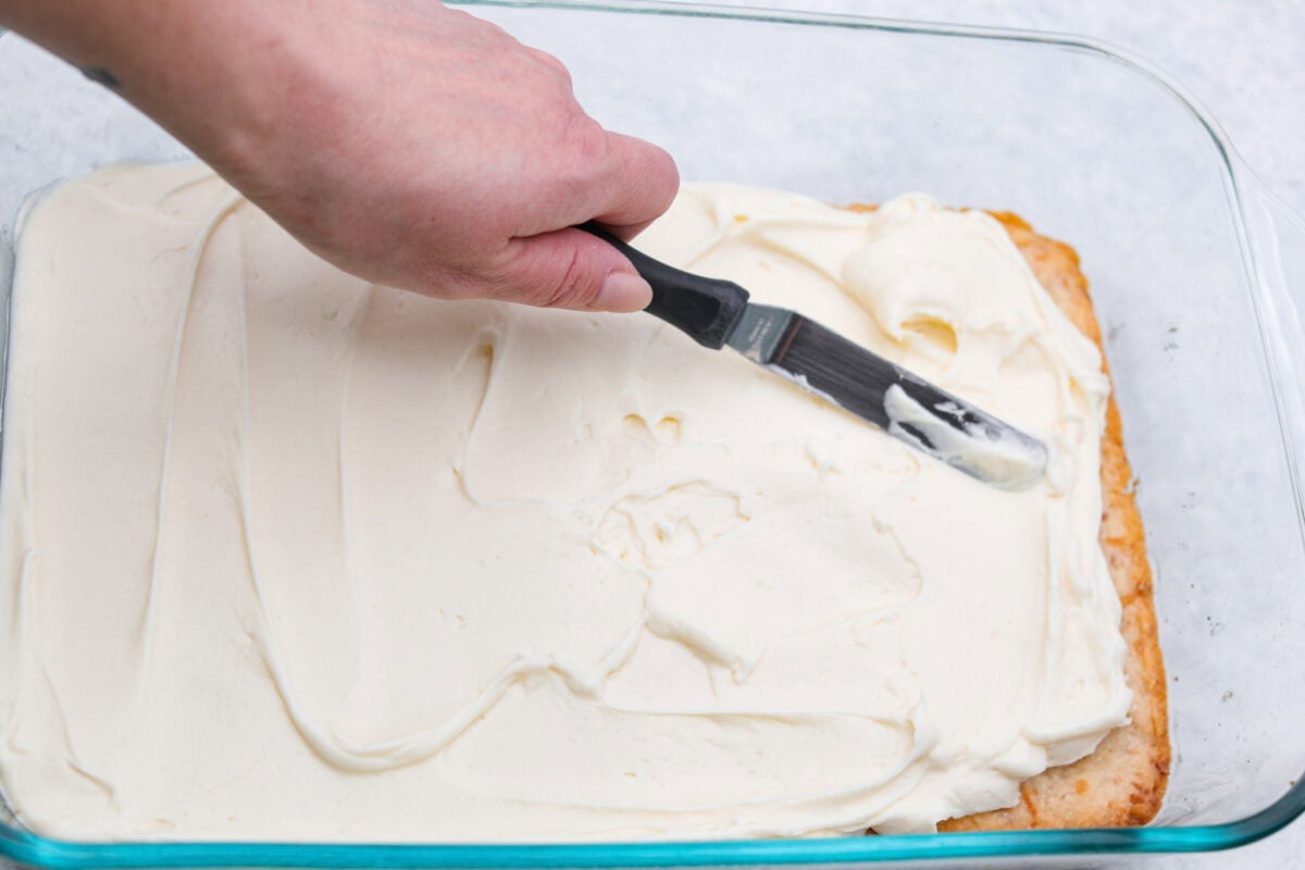 Someone spreading the cream cheese mixture on top of he crust. 